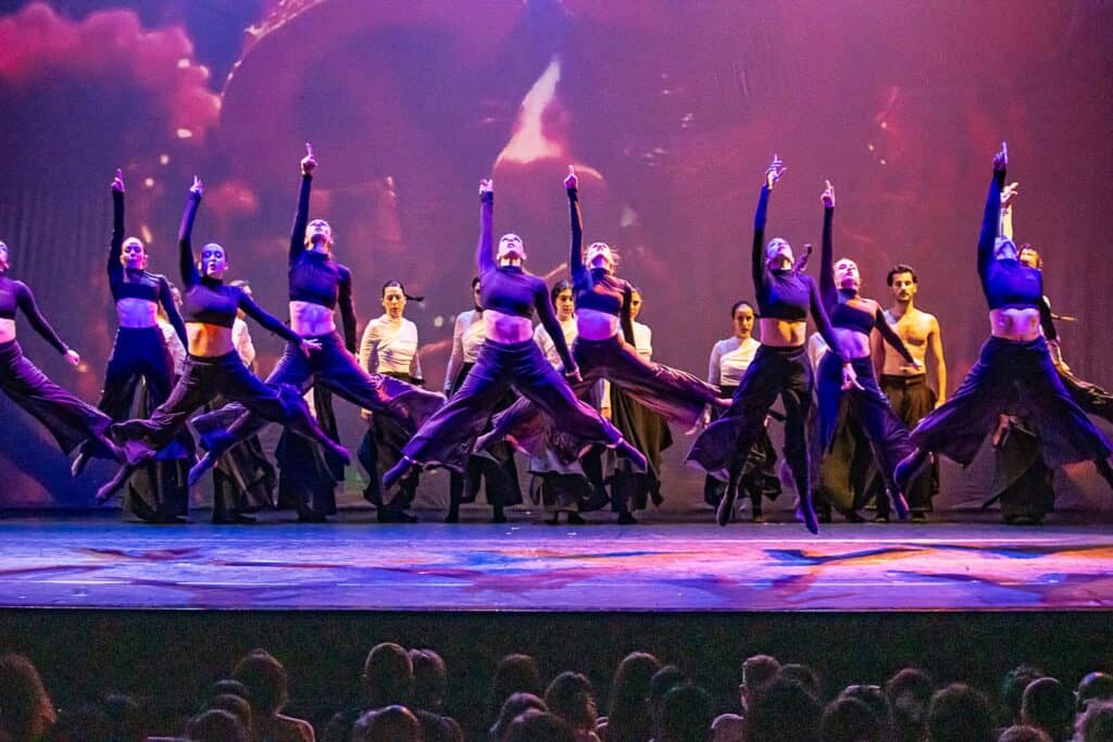 Three confident dancers performing against a purple gradient backdrop, showcasing dynamic movement and individual style in artistic lighting