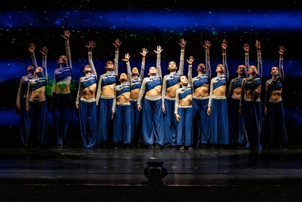Three confident dancers performing against a purple gradient backdrop, showcasing dynamic movement and individual style in artistic lighting