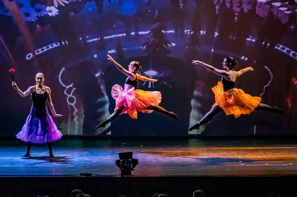 Three confident dancers performing against a purple gradient backdrop, showcasing dynamic movement and individual style in artistic lighting